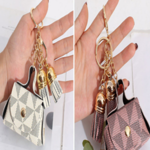 Set x2 llaveros de cuero sintético con monograma y borlas doradas; uno en tono crema y otro en rosa, sostenidos por manos.