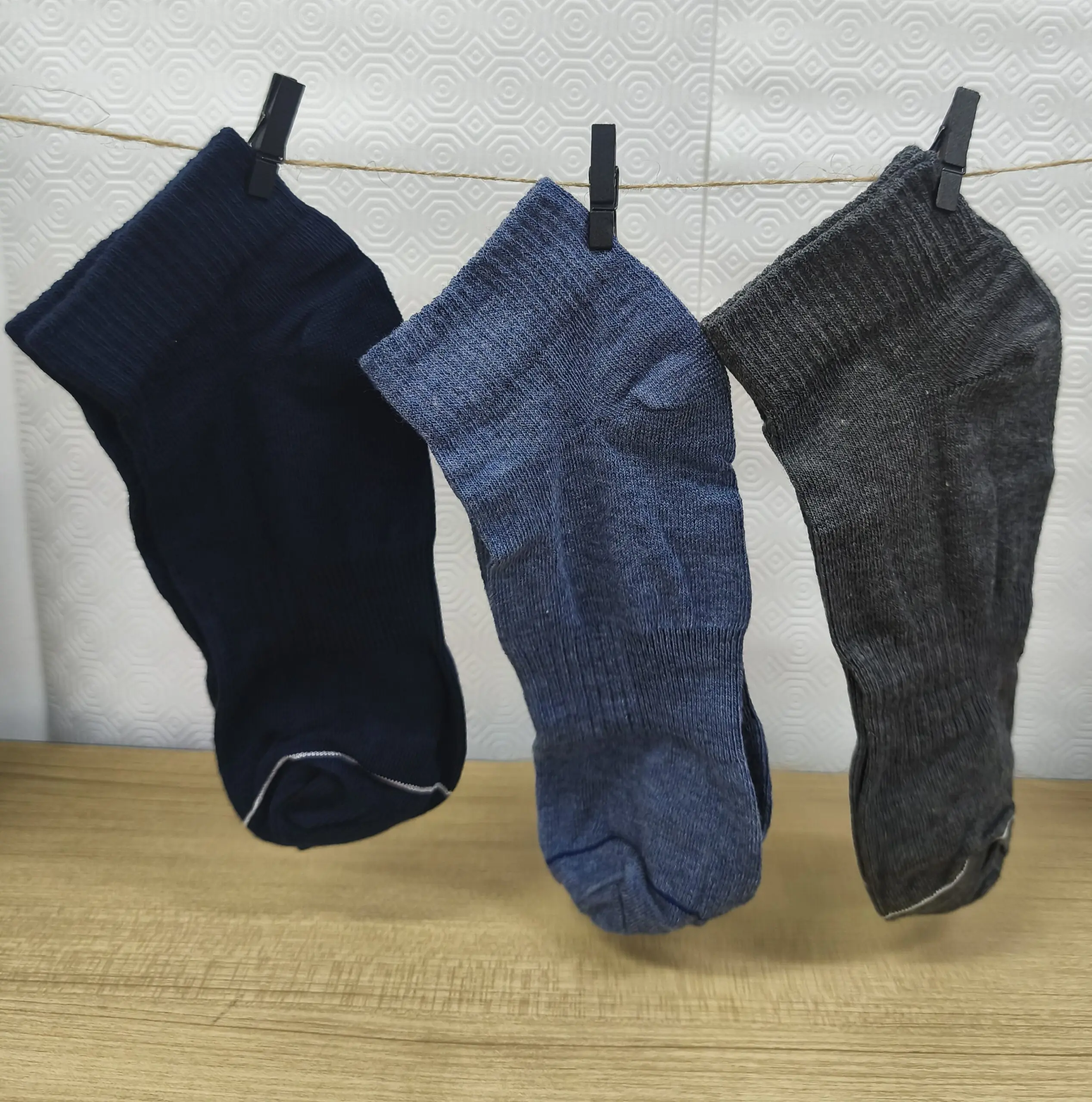 Pack de tres medias tobilleras de algodón en azul marino, azul medio y gris, colgadas de un cordel con pinzas negras sobre fondo claro.