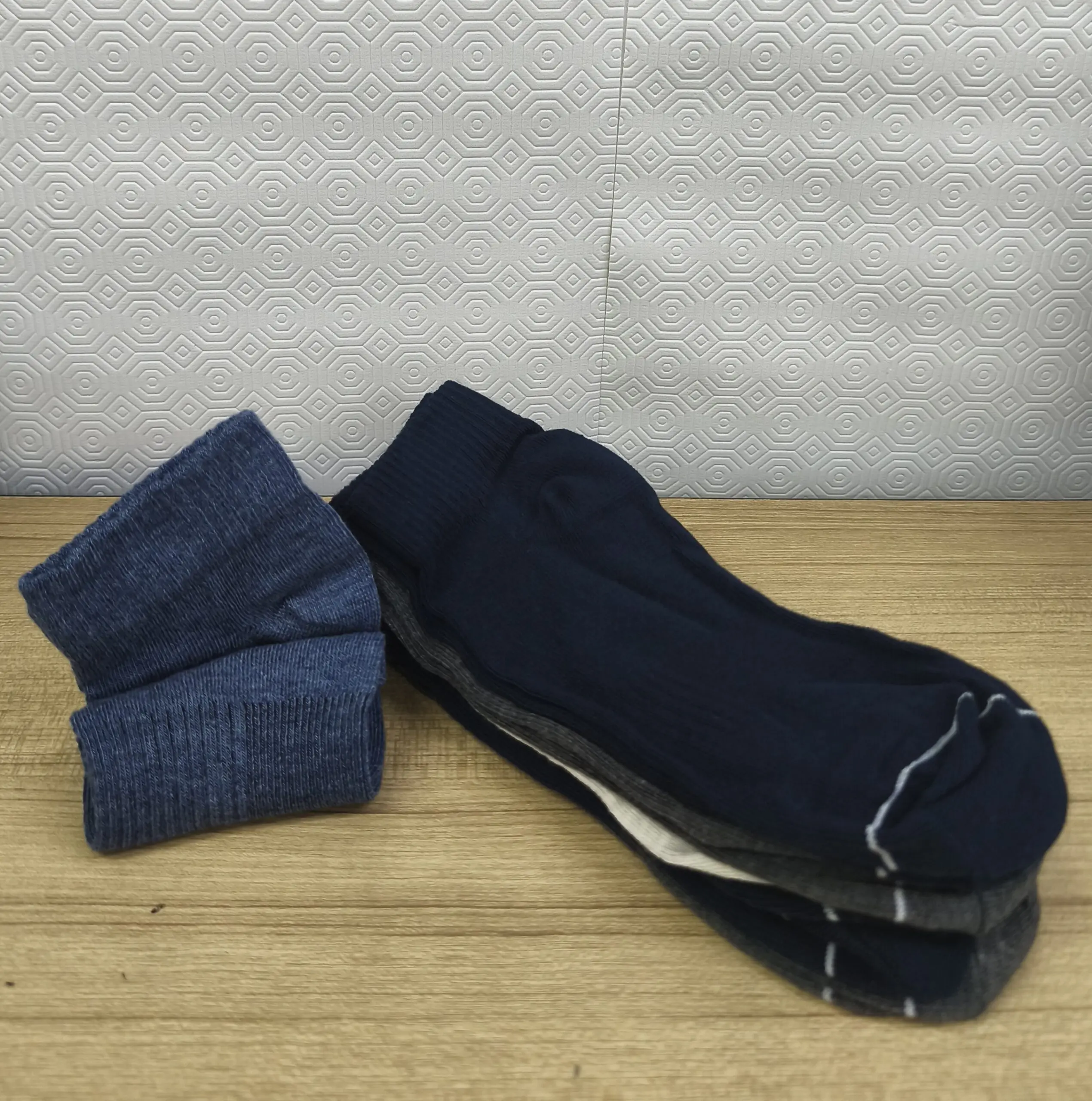Tres pares de medias tobilleras de algodón peinado en azul jaspeado, marino y gris con borde acanalado, sobre una superficie de madera.
