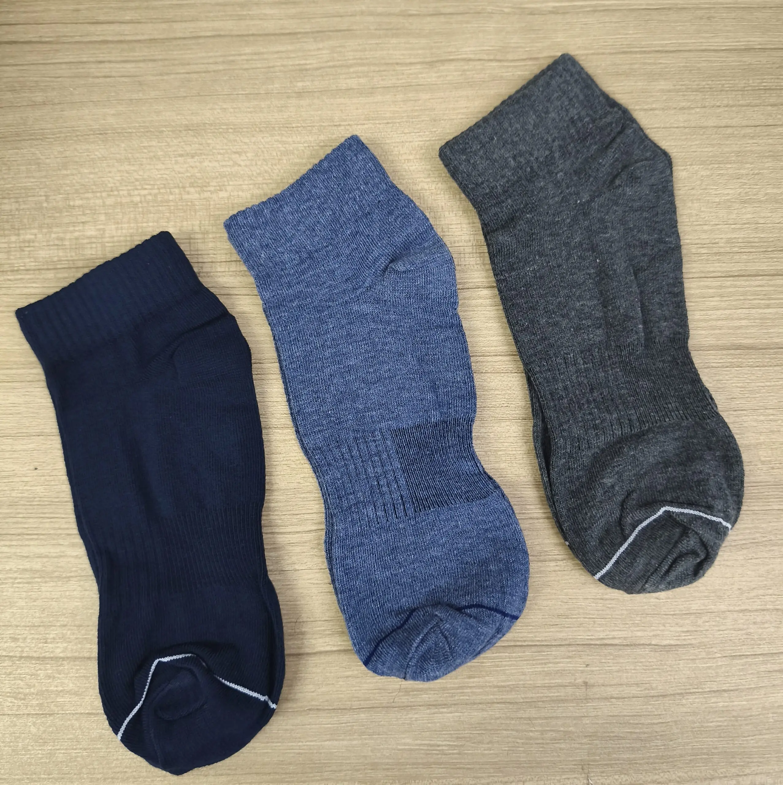 Pack de tres medias tobilleras de algodón en azul oscuro, azul medio y gris oscuro, sobre una superficie de madera clara.