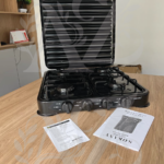 Estufa a gas Sokany negra de cuatro puestos sobre mesa de madera, con tapa protectora vertical ranurada y manuales incluidos en primer plano.