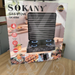 Caja de estufa a gas Sokany negra de cuatro puestos con tapa protectora vertical acanalada y mandos frontales sobre mesa de madera