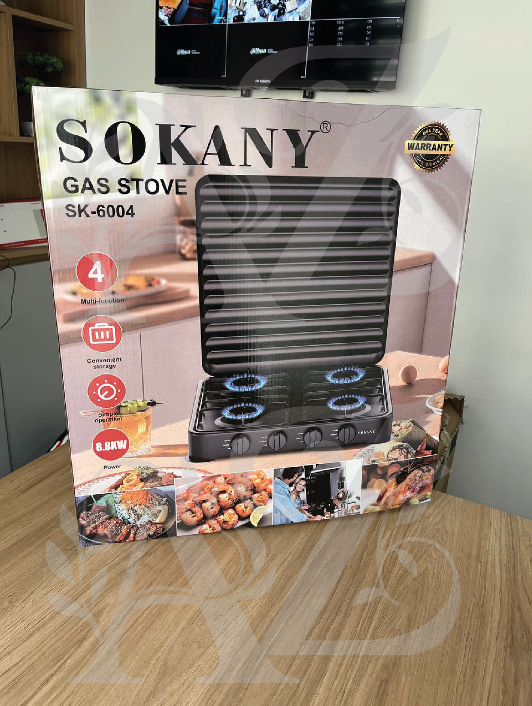 Caja de estufa a gas Sokany negra de cuatro puestos con tapa protectora vertical acanalada y mandos frontales sobre mesa de madera