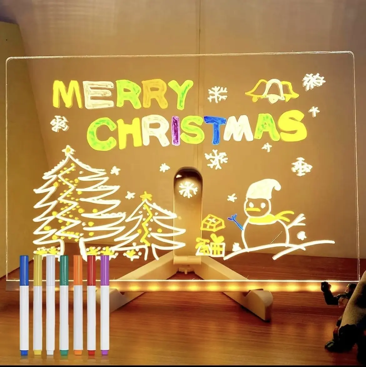 Tablero led de acrílico transparente con base de soporte, incluye seis marcadores de colores para crear dibujos navideños brillantes sobre la superficie.