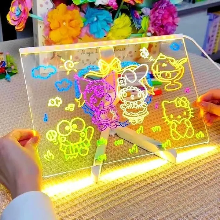 Tablero LED de acrílico transparente con dibujos de personajes Sanrio iluminados en neón, sostenido por manos sobre un soporte de madera en mesa.