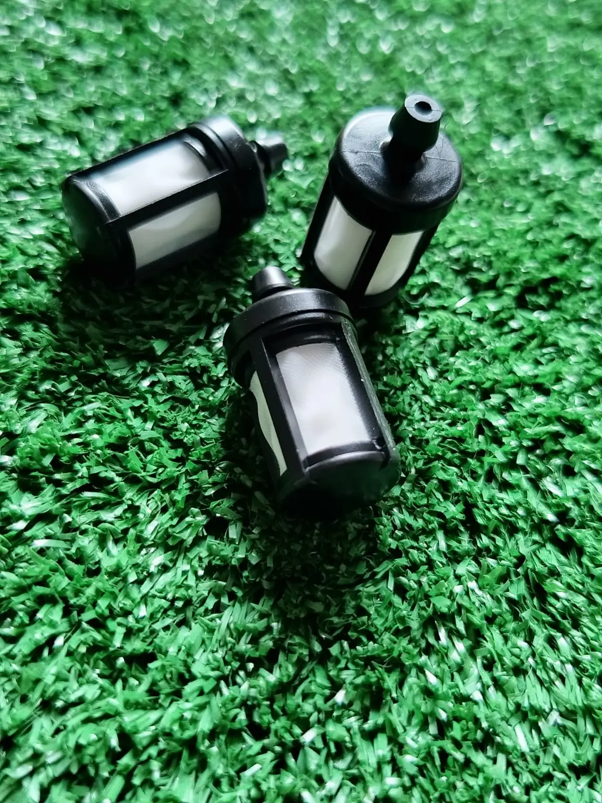 Tres filtros de combustible negros para motosierras Stihl MS382 y MS381 con malla filtrante blanca, dispuestos sobre una superficie de césped artificial.