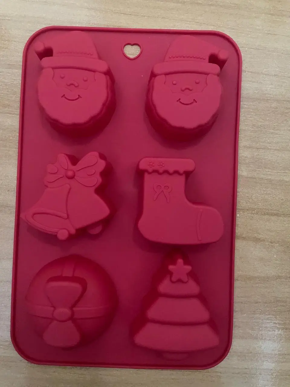 Molde de silicona rojo con seis cavidades de figuras navideñas: rostros de Santa Claus, campana, calcetín, esfera y árbol con estrella.