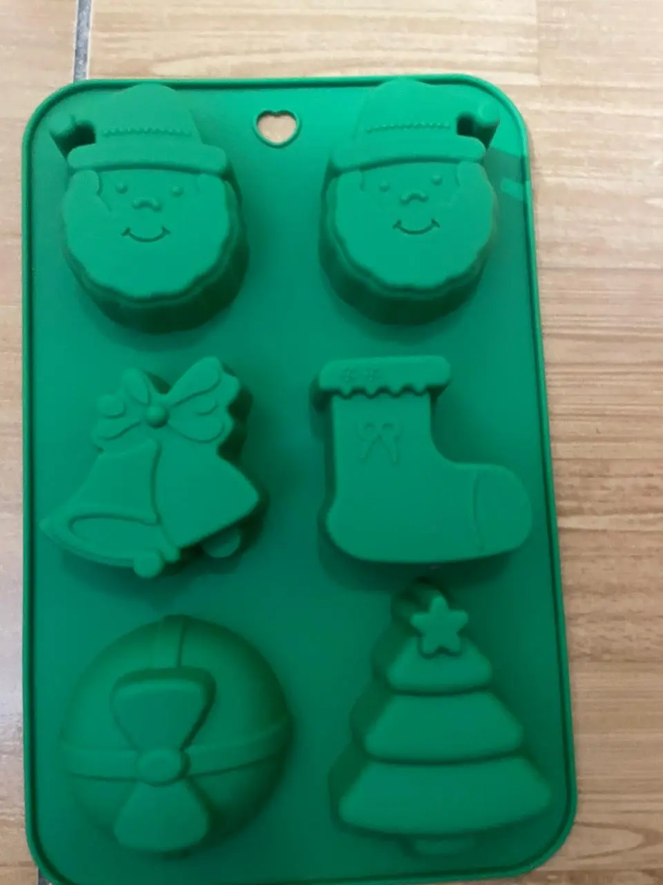 Molde de silicona verde con seis cavidades de figuras navideñas: dos caras de Santa, un cascabel, un calcetín, una esfera y un árbol.