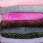 Pila de cobijas tipo piña suaves y ligeras en colores azul, rosado, gris, fucsia, café, verde oscuro, lila y negro.