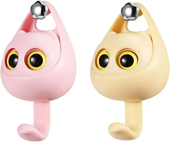 Dos ganchos de pared autoadhesivos con diseño de gato interactivo en colores rosa y beige, que abren los ojos al colgar objetos.