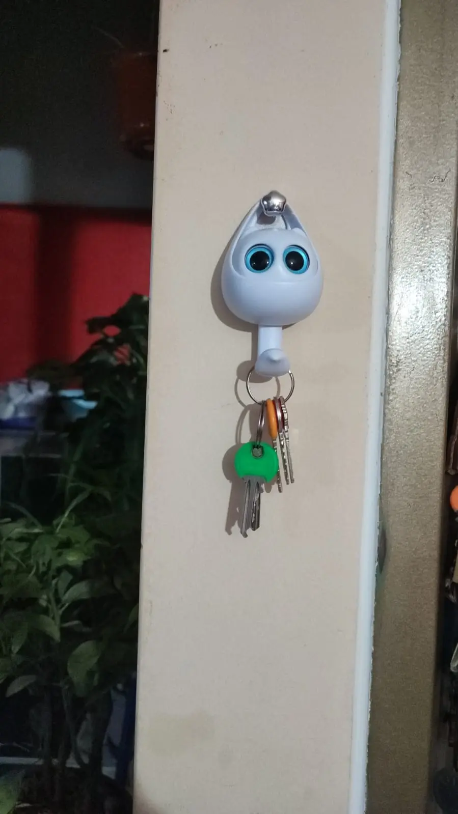 Porta llaves adhesivo blanco con diseño de gato y ojos azules, montado en pared beige con un manojo de llaves colgando.