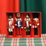 Caja roja con cuatro soldados cascanueces colgantes de madera en color rojo, azul y negro, sobre mantel a cuadros verde y rojo.