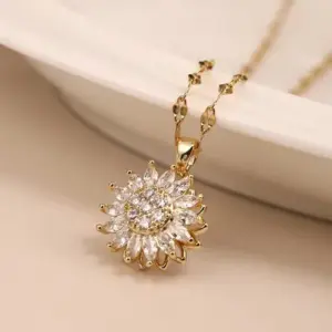 Collar dorado con dije de girasol adornado con circonitas brillantes y cadena fina sobre fondo crema.