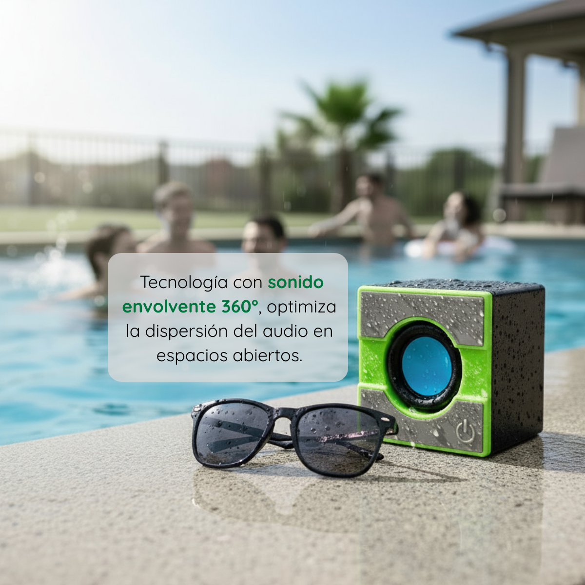 Mini parlante portátil Bluetooth verde y negro junto a gafas de sol al borde de una piscina con personas disfrutando al fondo