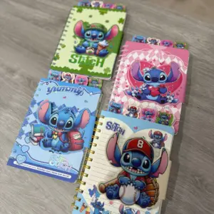Cuatro libretas espiraladas con diseños temáticos de Stitch en colores verde, rosado y azul, dispuestas sobre superficie de madera.