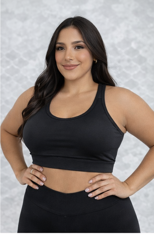 Top deportivo negro de soporte firme para tallas plus, con escote redondo y tirantes anchos, usado por modelo en plano medio frontal.