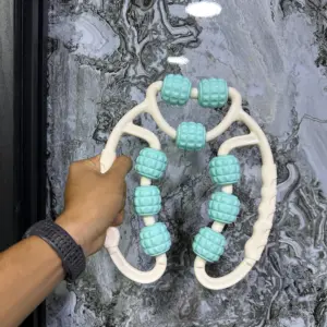 Rodillo de masaje manual con estructura blanca y rodillos texturizados color turquesa, sostenido por una mano sobre fondo de mármol gris.