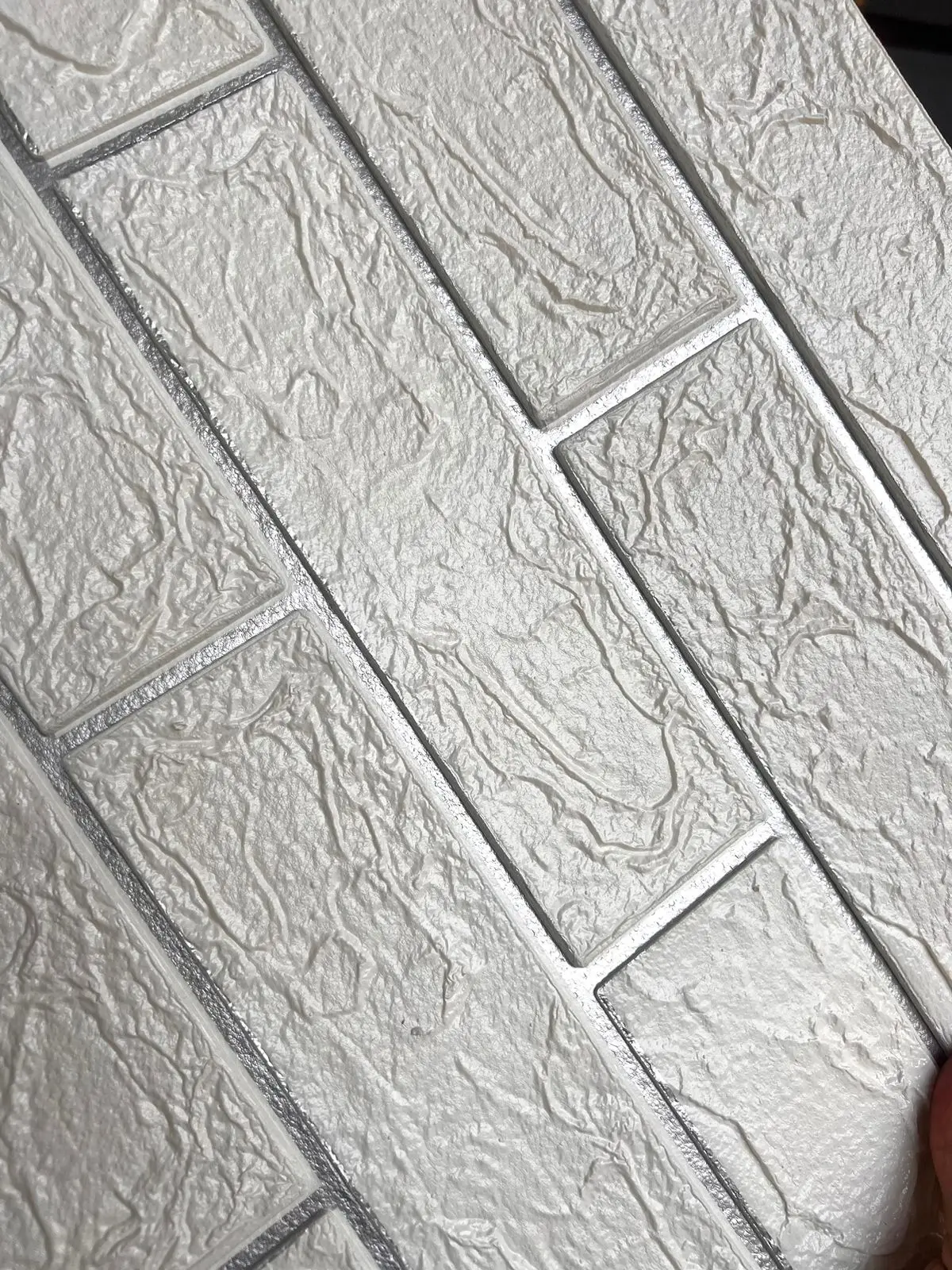 Primer plano de panel adhesivo de pared con diseño de ladrillo plata y relieve 3D de textura rugosa y detallada.
