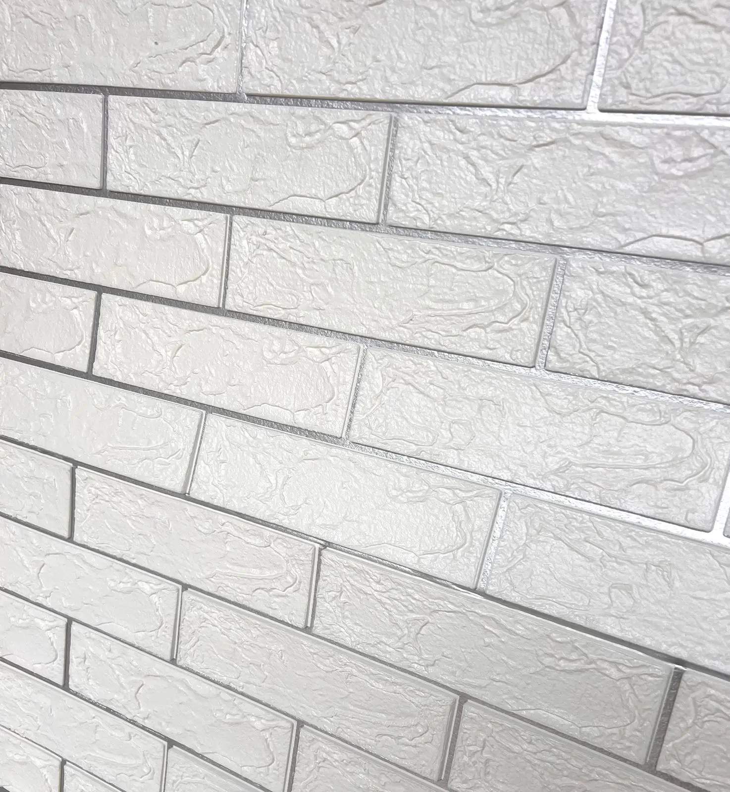 Panel adhesivo de pared con diseño de ladrillo plata en relieve 3D y textura rugosa para revestimiento decorativo de muros.