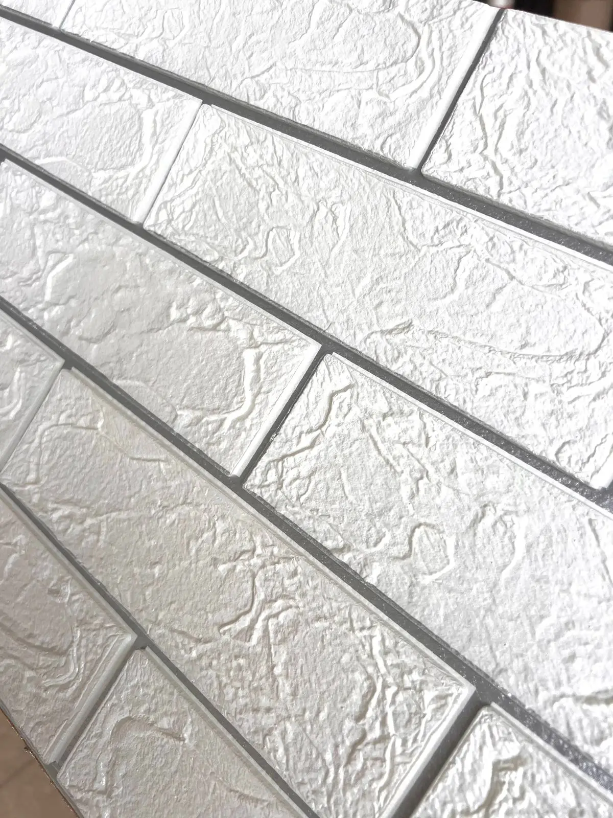 Panel adhesivo de pared diseño ladrillo en color plata con textura rugosa y relieve 3D, mostrado en primer plano.