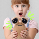 Peluche beige de Pou con grandes ojos saltones negros y brillantes, sostenido por una niña sorprendida. Textura suave y diseño compacto.