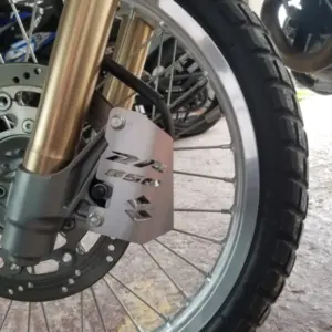 Protector de cáliper de freno en acero inoxidable con grabado DR 650 y Suzuki instalado en la rueda delantera de una motocicleta.