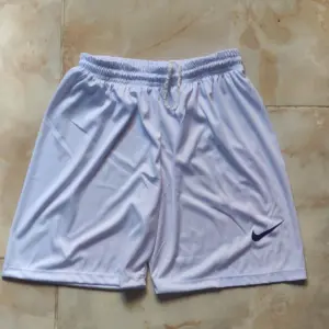 Pantaloneta deportiva blanca de fútbol con cordón ajustable en la cintura y el isotipo de la marca en la pierna derecha.