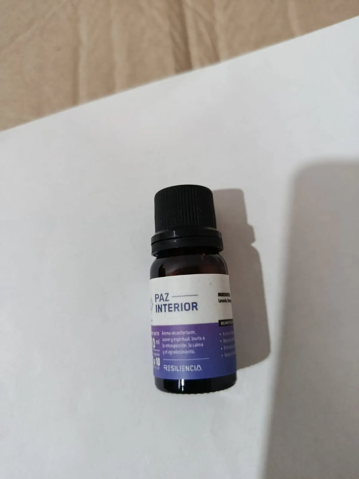 Frasco de vidrio ámbar de 10 ml con tapa negra, etiqueta blanca y morada que identifica el aceite esencial Paz Interior de la marca Resiliencia.