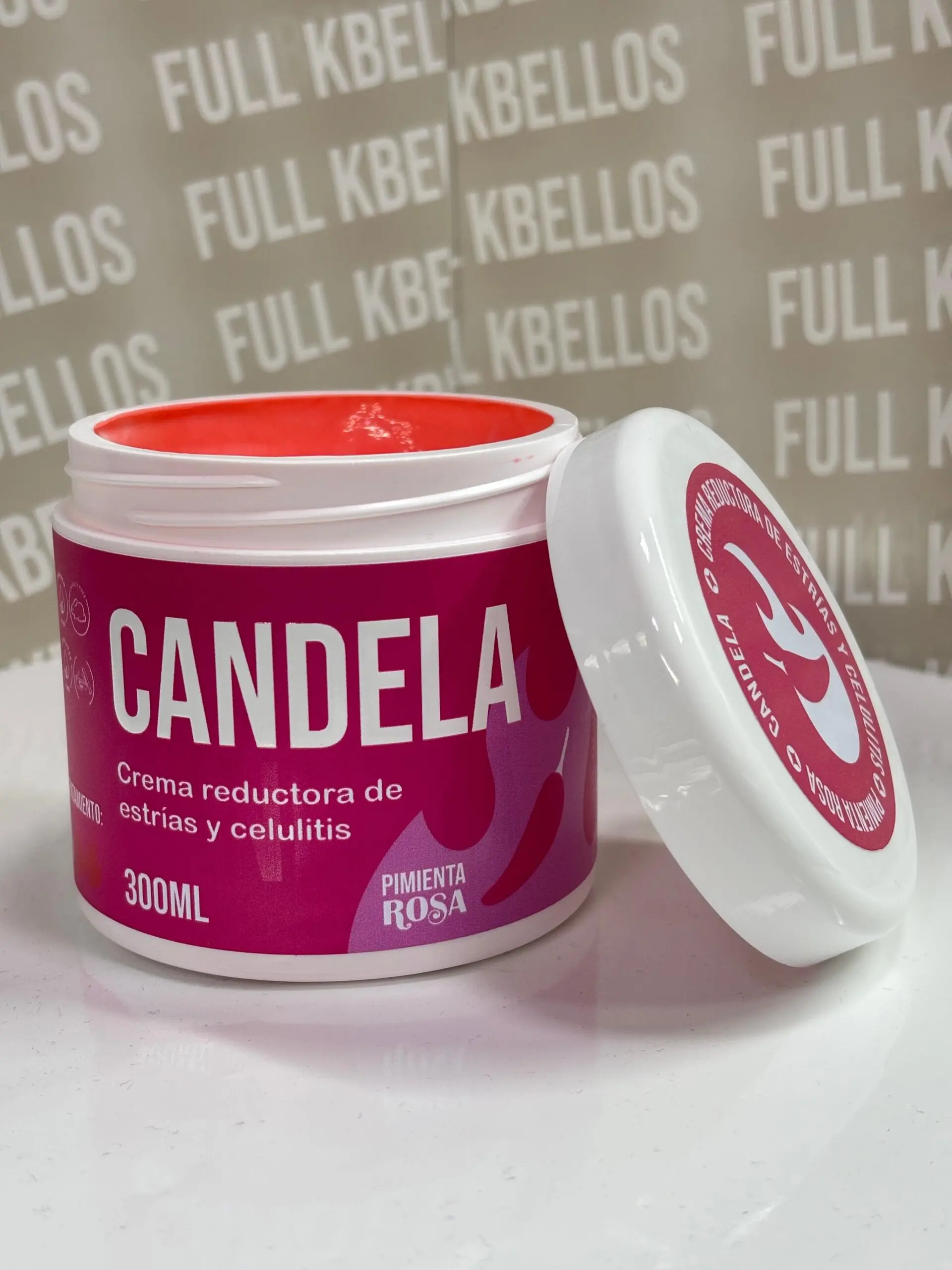 Frasco blanco y fucsia de 300 ml de crema reductora anticelulitis Candela con extracto de pimienta rosa, abierto y con tapa al lado sobre superficie blanca.
