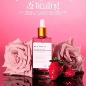 Aceite hidratante para después del afeitado en botella cuadrada con gotero dorado, rodeado de rosas rosadas y fresas frescas sobre superficie reflectante.