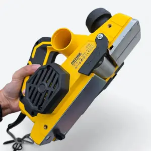Cepillo eléctrico para madera amarillo de mano, mostrando su suela metálica, cuchillas y salida de extracción de viruta.
