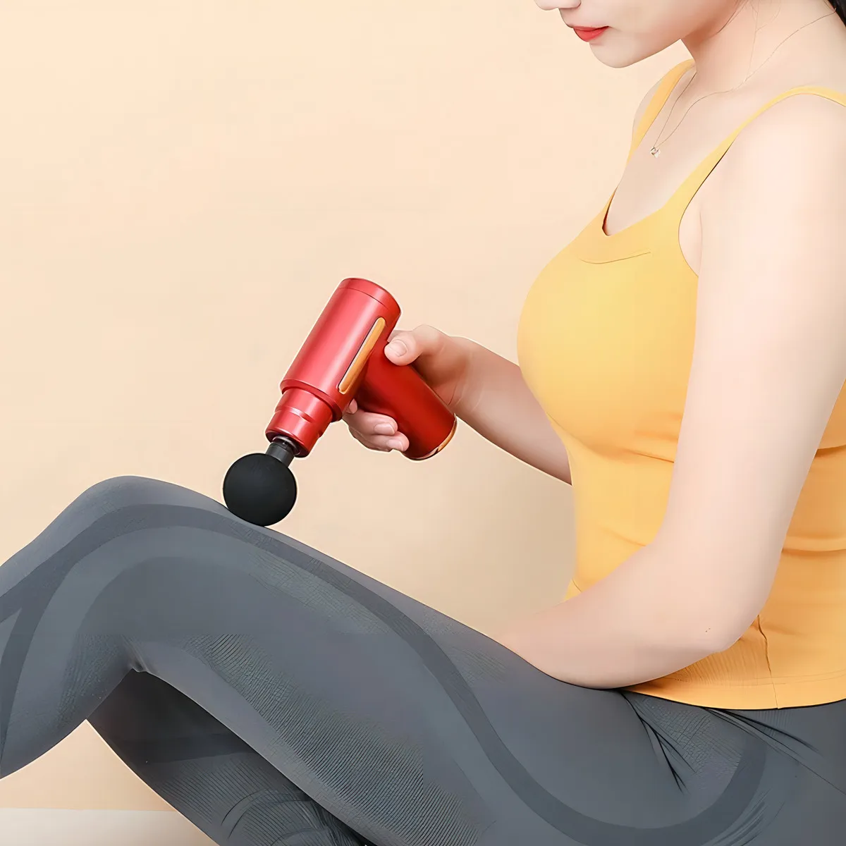 Mujer usando mini masajeador manual rojo con cabezal esférico negro sobre su muslo para aliviar la tensión muscular.