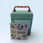 Botilito verde tipo maleta con asa naranja, diseño acanalado y lámina de calcomanías con temática de viaje al frente.