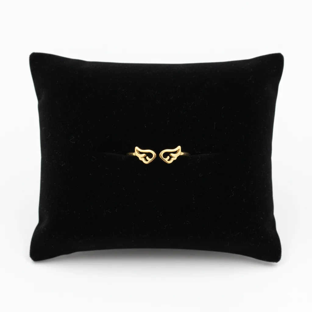 Anillo de acero inoxidable dorado con diseño de alas simétricas, presentado sobre un cojín de terciopelo negro.