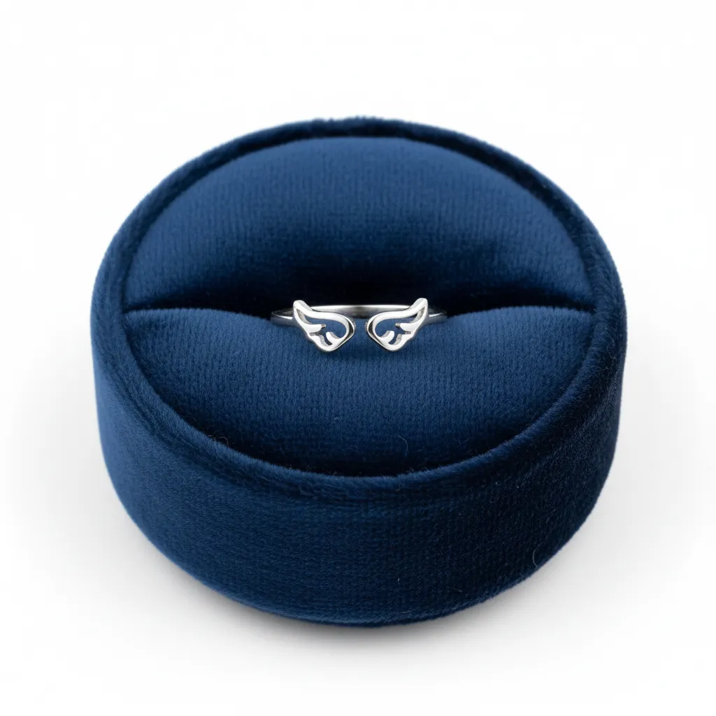 Anillo minimalista de acero inoxidable con diseño de alas plateadas, presentado en un estuche de terciopelo azul oscuro.