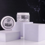 Dos envases blancos de cera para cabello Rolda con acabado mate y fijación media, sobre bloques geométricos morados.