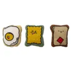 Set de tres juguetes de peluche texturizados para perros: un huevo frito, una galleta con cara y una tostada con mermelada, ideales para juego interactivo.