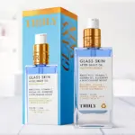Frasco rectangular de vidrio con aceite corporal azul y dispensador dorado junto a su caja de empaque celeste con letras naranjas.