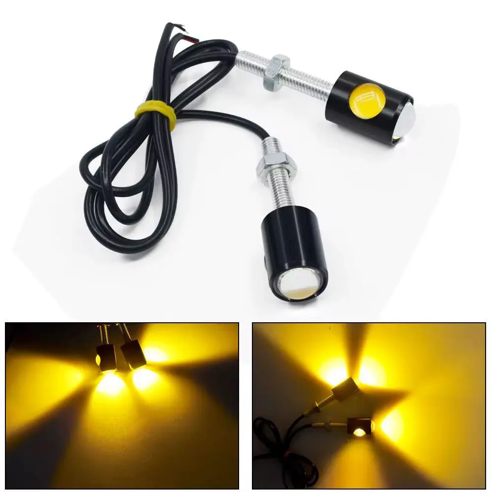 Par de direccionales LED negros con pernos de montaje y cables, mostrando su luz amarilla intensa y el patrón de iluminación proyectado.