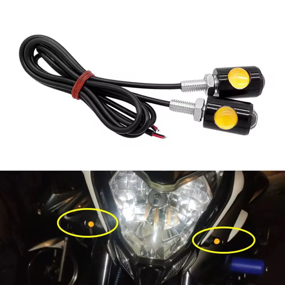 Par de direccionales LED ojos de águila negros con lente amarillo y cables largos, mostrados sueltos e instalados en el faro de una motocicleta.