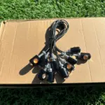 Direccionales LED ojos de águila amarillos con carcasa negra y cables, dispuestos en abanico sobre una caja de cartón en el césped.