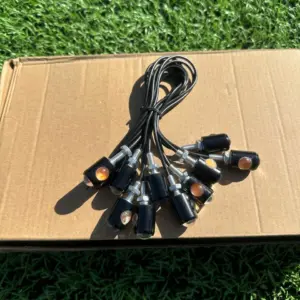 Direccionales LED ojos de águila amarillos con carcasa negra y cables, dispuestos en abanico sobre una caja de cartón en el césped.
