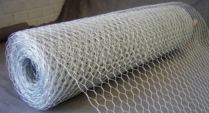 Rollo de malla metálica hexagonal galvanizada de tono plateado con textura de alambre tejido, desplegada sobre una superficie oscura.