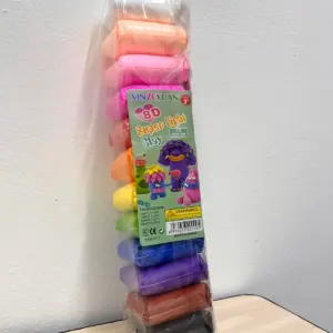 Paquete vertical de masa moldeable ligera con doce colores apilados, desde blanco superior hasta negro inferior, sobre una mesa de madera clara.