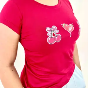 Camiseta roja de piel de durazno con estampado de cerezas con lazo rosa y fresas, de corte ajustado y cuello redondo.