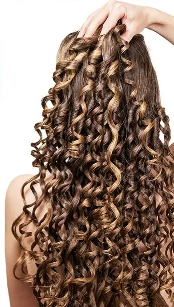 Cabello largo, castaño y con rizos definidos tipo tirabuzón, con reflejos dorados y textura hidratada.