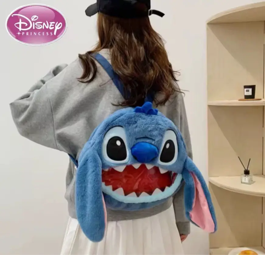 Bolso de peluche azul con diseño de Stitch, de textura suave, orejas largas y boca abierta, usado como mochila sobre un suéter gris.
