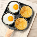 Sartén antiadherente negro con mango de madera y cuatro compartimentos con huevos y panqueques dorados, vista cenital sobre un mantel claro.
