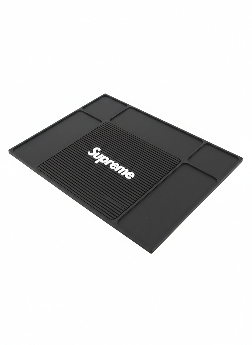 Tapete organizador negro para barbería con logo Supreme, superficie con textura de surcos y compartimentos rectangulares para herramientas.
