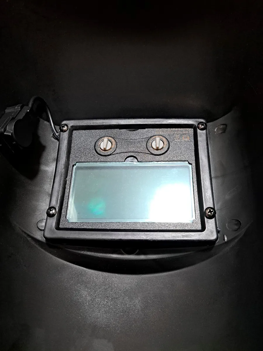 Vista interna de careta de soldadura negra con visor rectangular autooscurecible de tono azulado y tornillos de ajuste.